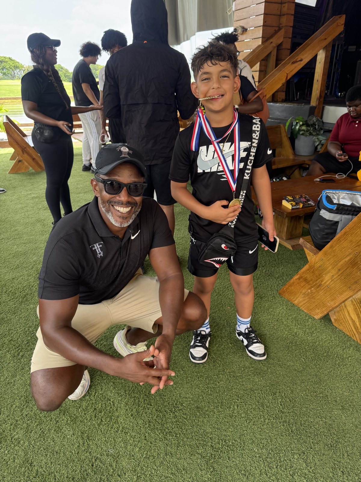 FFGF coach kneeling beside a youth participant wearing a medal at a golf program awards moment
